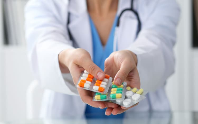 Female doctor hand holding pack of different tablet blisters closeup. Life save service, legal drug store, prescribe medicament, blood pressure, disease healing concept.